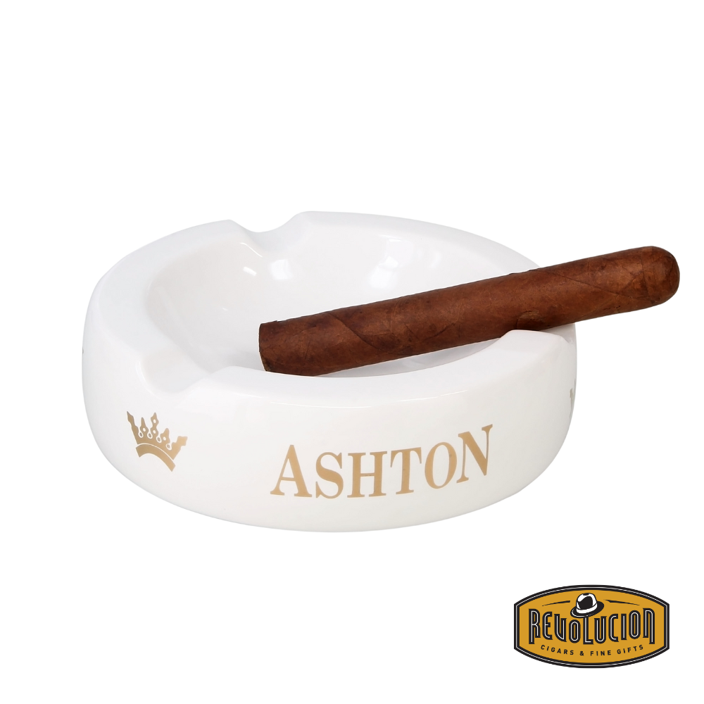 Ashton Large White Ashtray featuring a sleek finish with four cigar grooves and the iconic Ashton logo, holding a cigar with Revolucion Cigar & Fine Gifts logo.