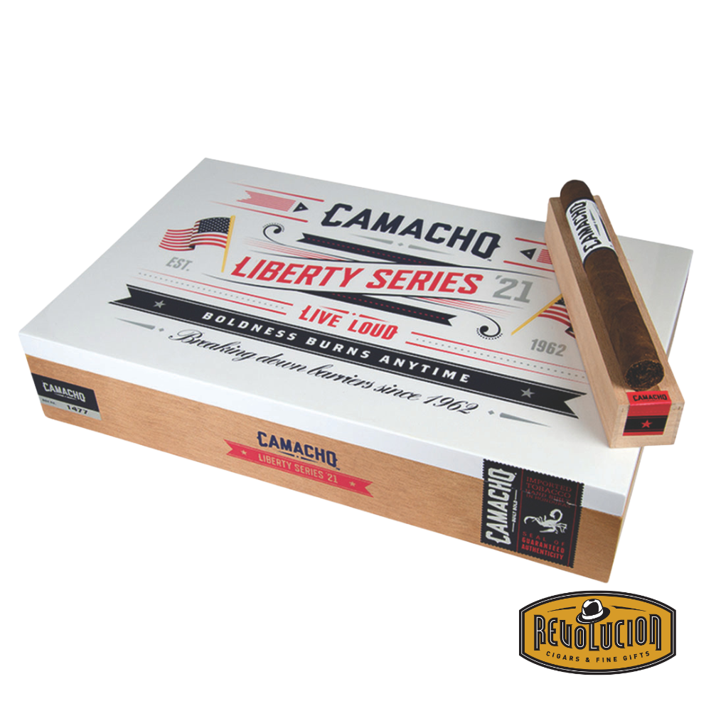Camacho Liberty 2021 Churchill cigar placed next to its open commemorative box showing multiple cigars inside.