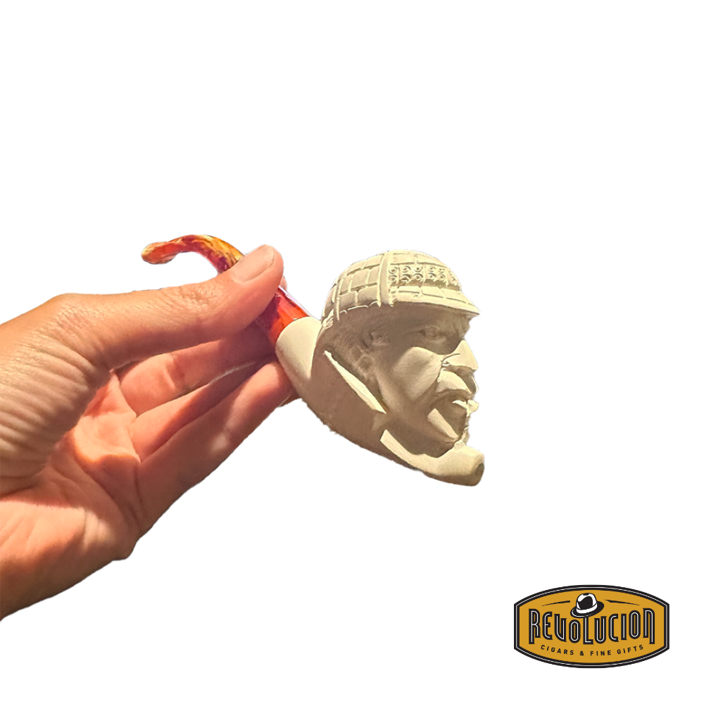A hand holding a Meerschaum pipe with a carved face of a man wearing a helmet. The pipe is cream-colored with intricate carvings, shown from a side view.