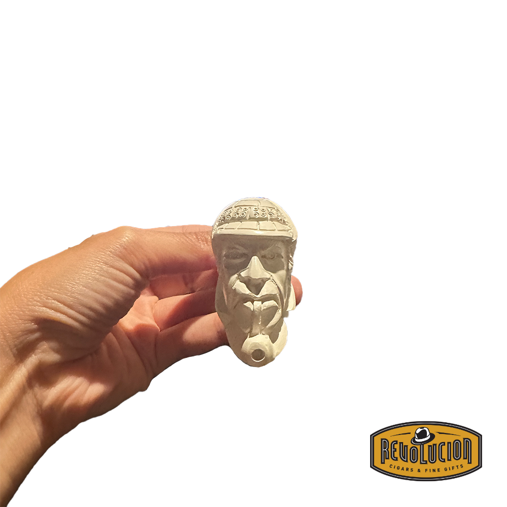 A hand holding a Meerschaum pipe with a carved face of a man wearing a helmet. The pipe is cream-colored and showcases intricate facial details from the front view.