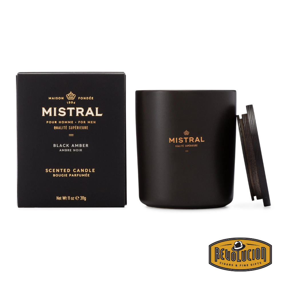 Black Mistral candle in an elegant black jar with a wooden lid, featuring the label ‘Black Amber - Pour Homme’ and a matching box showcasing the same branding. The image includes the Revolucion Cigars & Fine Gifts logo
