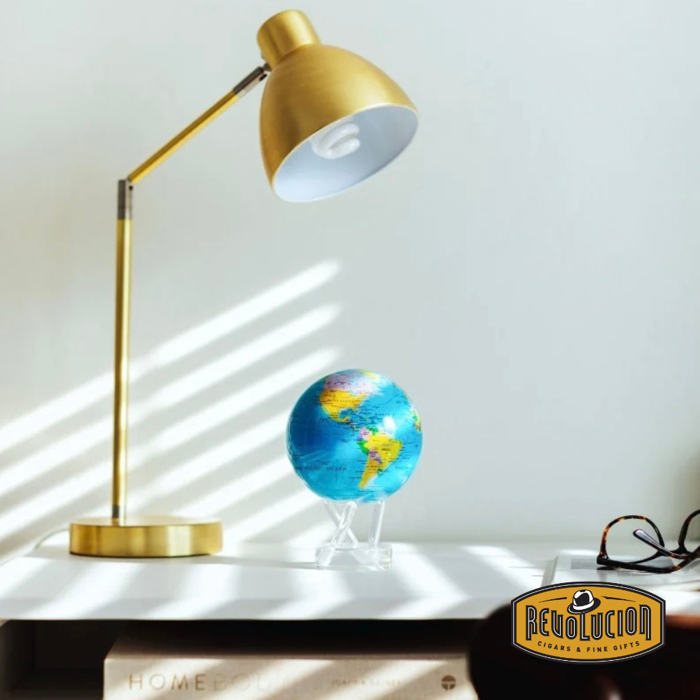The Mova Blue Political World Globe (4.5") elegantly displayed on a white desk, accompanied by a gold lamp and reading glasses, adding a sophisticated touch to the decor.