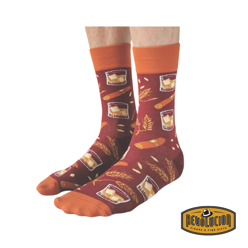 A pair of Uptown calf-length cotton unisex socks featuring a rich burgundy base with orange cuffs, toes, and heels. The design showcases whiskey glasses with ice, cigars, and wheat accents, evoking a luxurious and classic aesthetic.