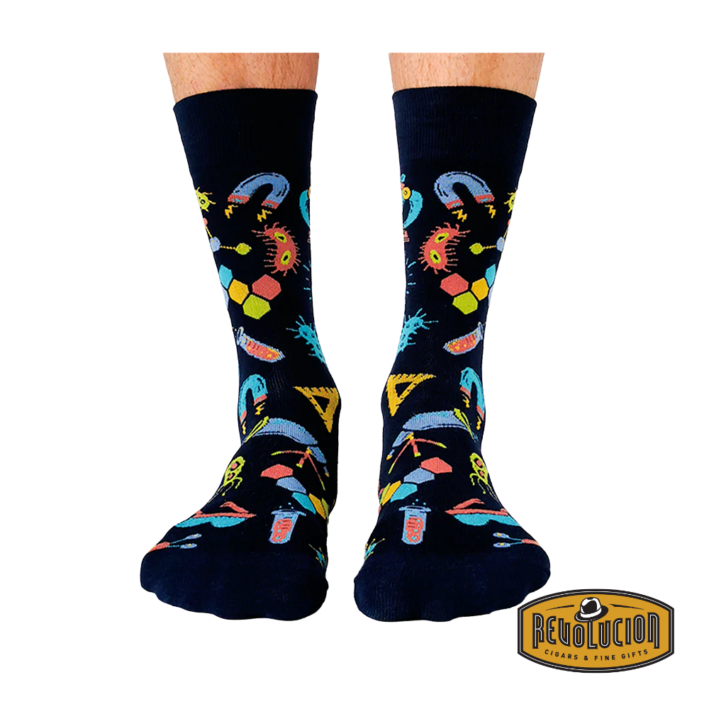 Front view of black socks featuring colorful science-themed graphics including test tubes, molecules, and magnifying glasses. The socks are branded with the Revolucion Cigars & Fine Gifts logo.