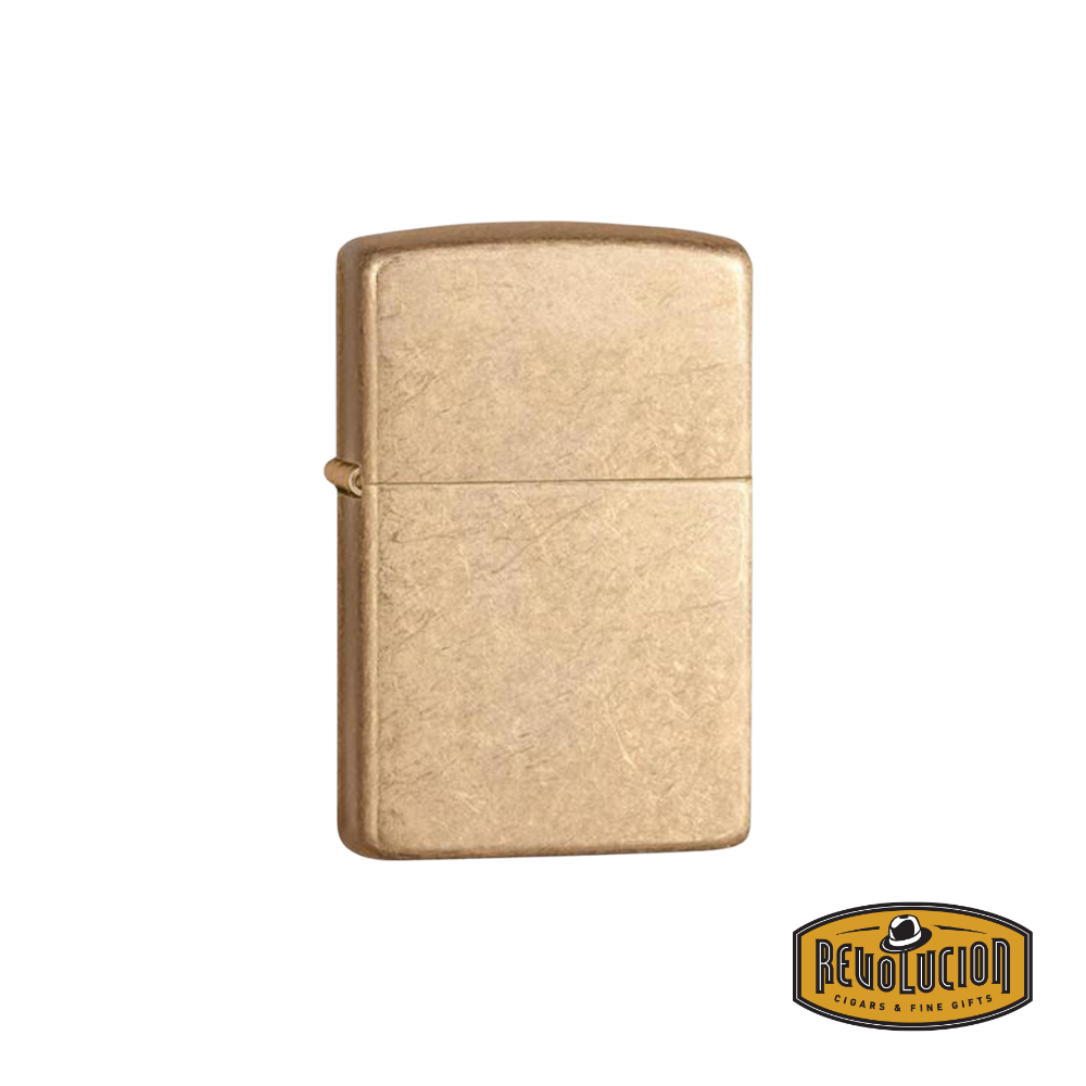 A Zippo Armor Tumbled Brass Lighter with a rugged, textured brass finish. The sturdy Armor case adds durability and a bold aesthetic. The Revolucion Cigars & Fine Gifts logo is positioned in the corner.