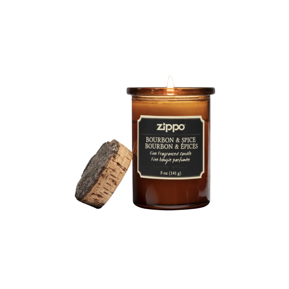 Zippo Bourbon & Spice Candle in an amber glass jar with a cork lid, emitting a warm glow. The label displays the fragrance name and weight in both English and French.