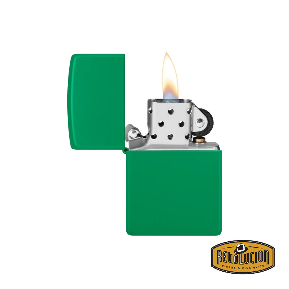 A Zippo lighter in a vibrant grass green matte finish, opened with a visible flame. The classic metal interior and flint wheel mechanism are exposed, showcasing its iconic design. The "Revolucion Cigars & Fine Gifts" logo is placed in the bottom right corner.
