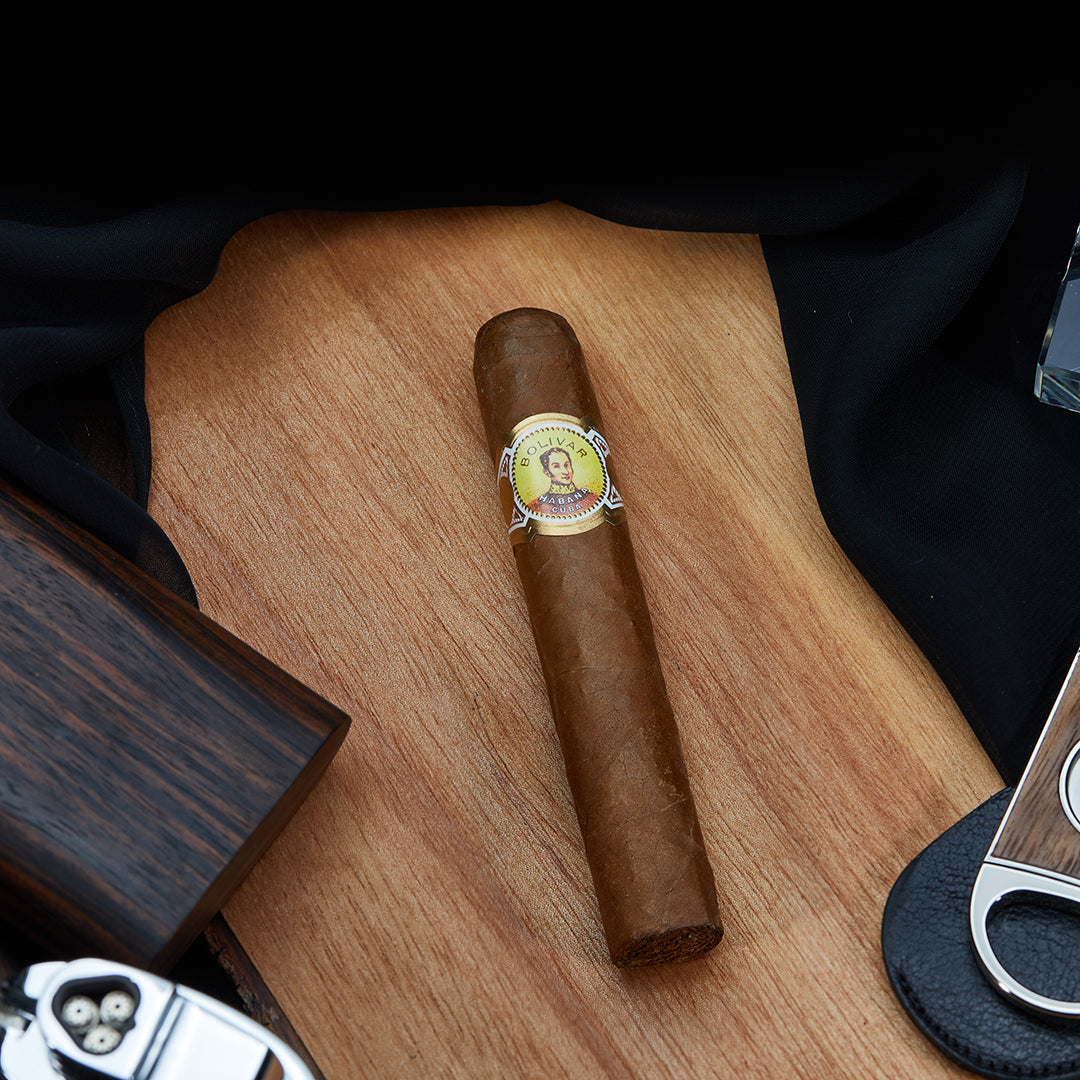 A Bolivar Royal Corona robusto cigar placed on a wooden surface, surrounded by cigar accessories, highlighting its premium construction.
