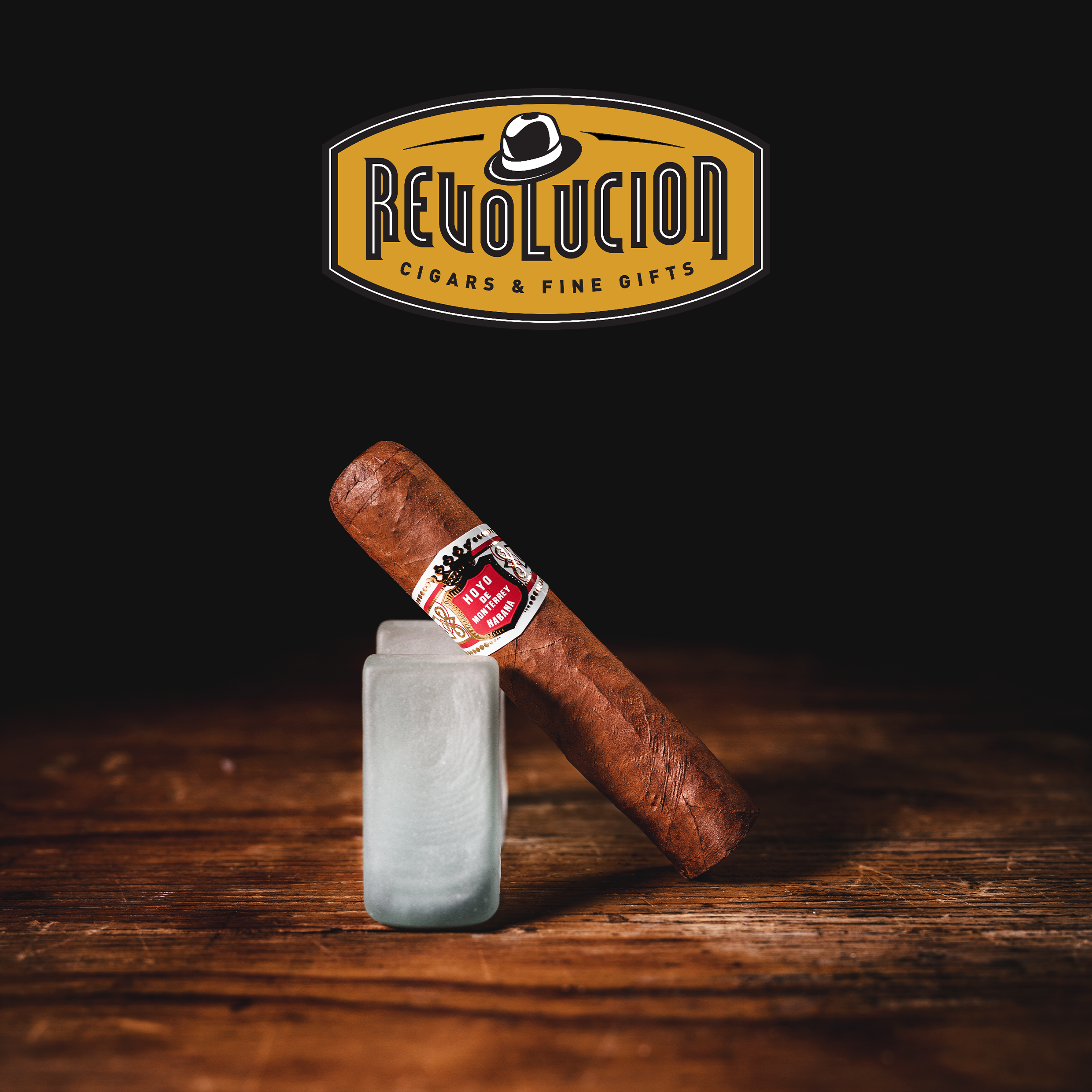 A Hoyo de Monterrey Petit Robusto Cuban cigar displayed at an angle, showcasing its smooth, golden-brown wrapper and detailed red-and-white band.