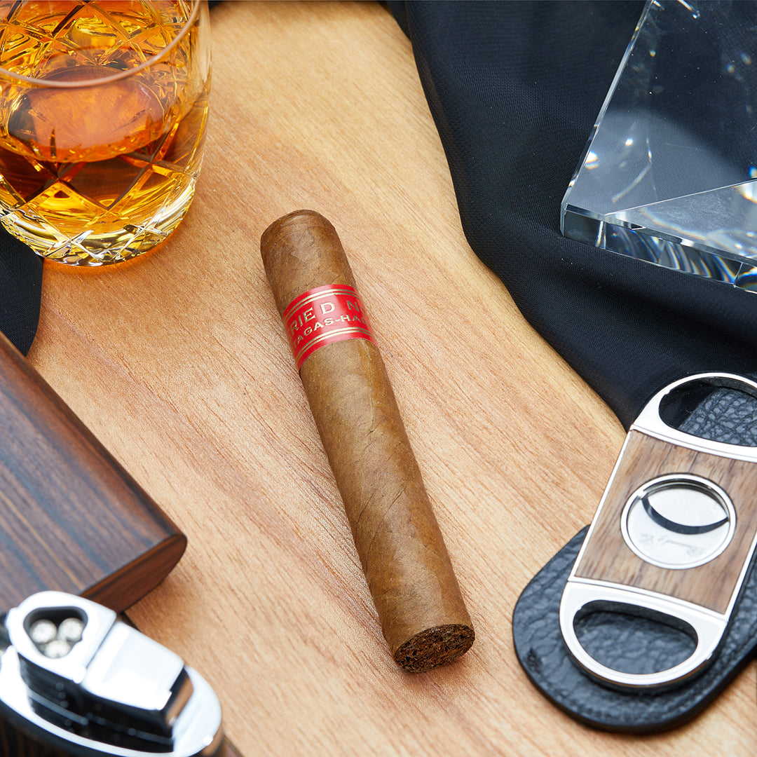Partagás Serie D No. 4 Cuban cigar with a red band, placed on a wooden surface alongside a whiskey glass, a cigar cutter, and other smoking accessories.
