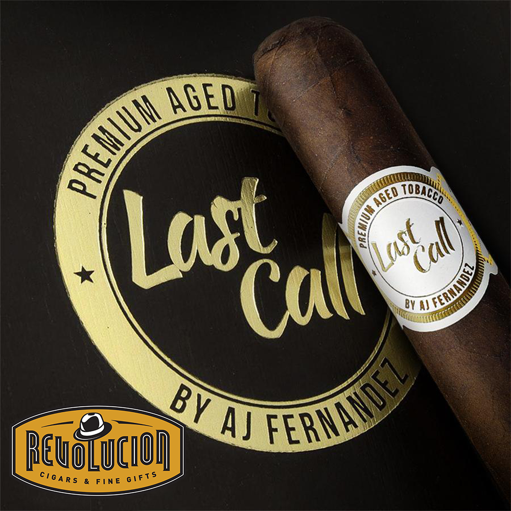 AJ Fernandez Last Call Geniales Maduro cigar placed diagonally on a black surface, with the cigar's white and gold band and the 'Last Call' logo prominently displayed in the background