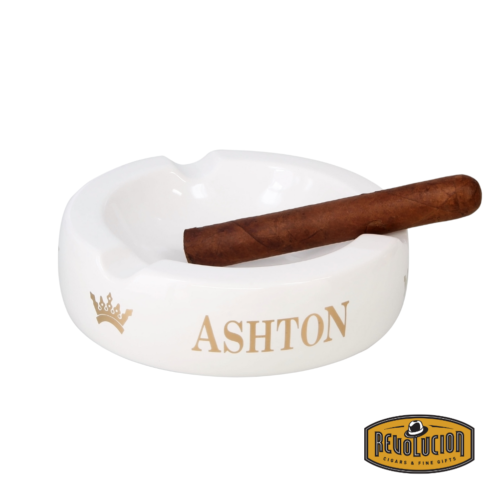 Ashton Large White Ashtray featuring a sleek finish with four cigar grooves and the iconic Ashton logo, holding a cigar with Revolucion Cigar &amp; Fine Gifts logo.