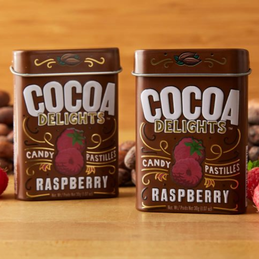 Two tins of Big Sky Mints Cocoa Delights Raspberry placed against a background of fresh strawberries, enhancing the fruity theme.