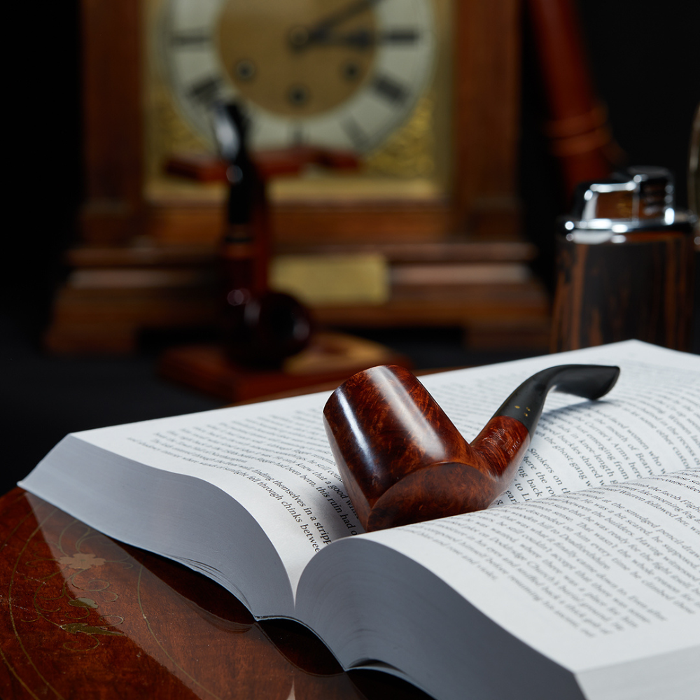 The Brigham Mountaineer #84 pipe resting on an open book, set in a refined study with vintage décor, emphasizing its classic design and elegant appeal for pipe enthusiasts.