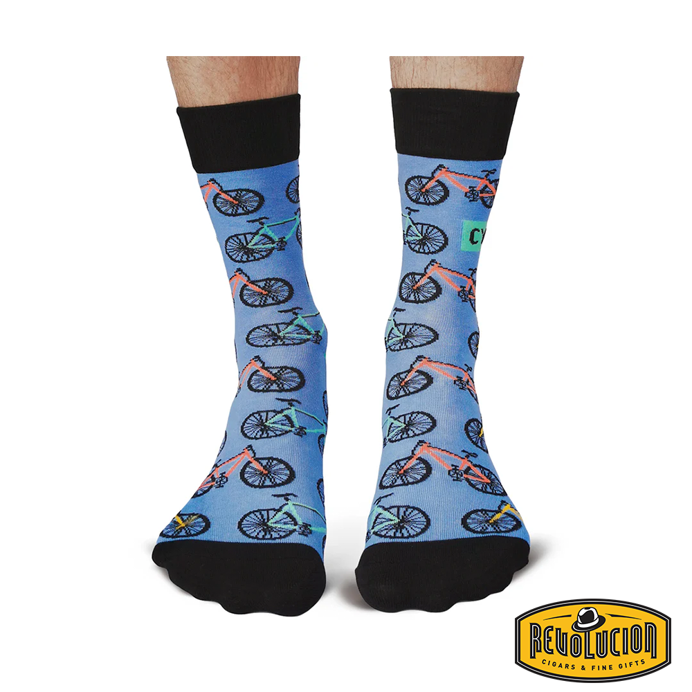 Front view of blue socks with colorful bicycle graphics and black cuffs and toes. The socks are branded with the Revolucion Cigars & Fine Gifts logo.