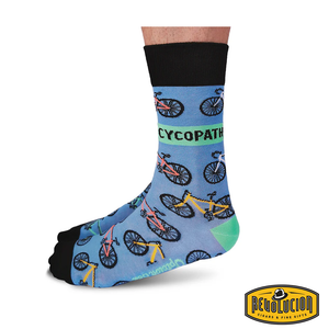 Side view of blue socks featuring colorful bicycle graphics and the word 'CYCOPATH' in bold green letters. The socks have black cuffs and toes and are branded with the Revolucion Cigars & Fine Gifts logo.