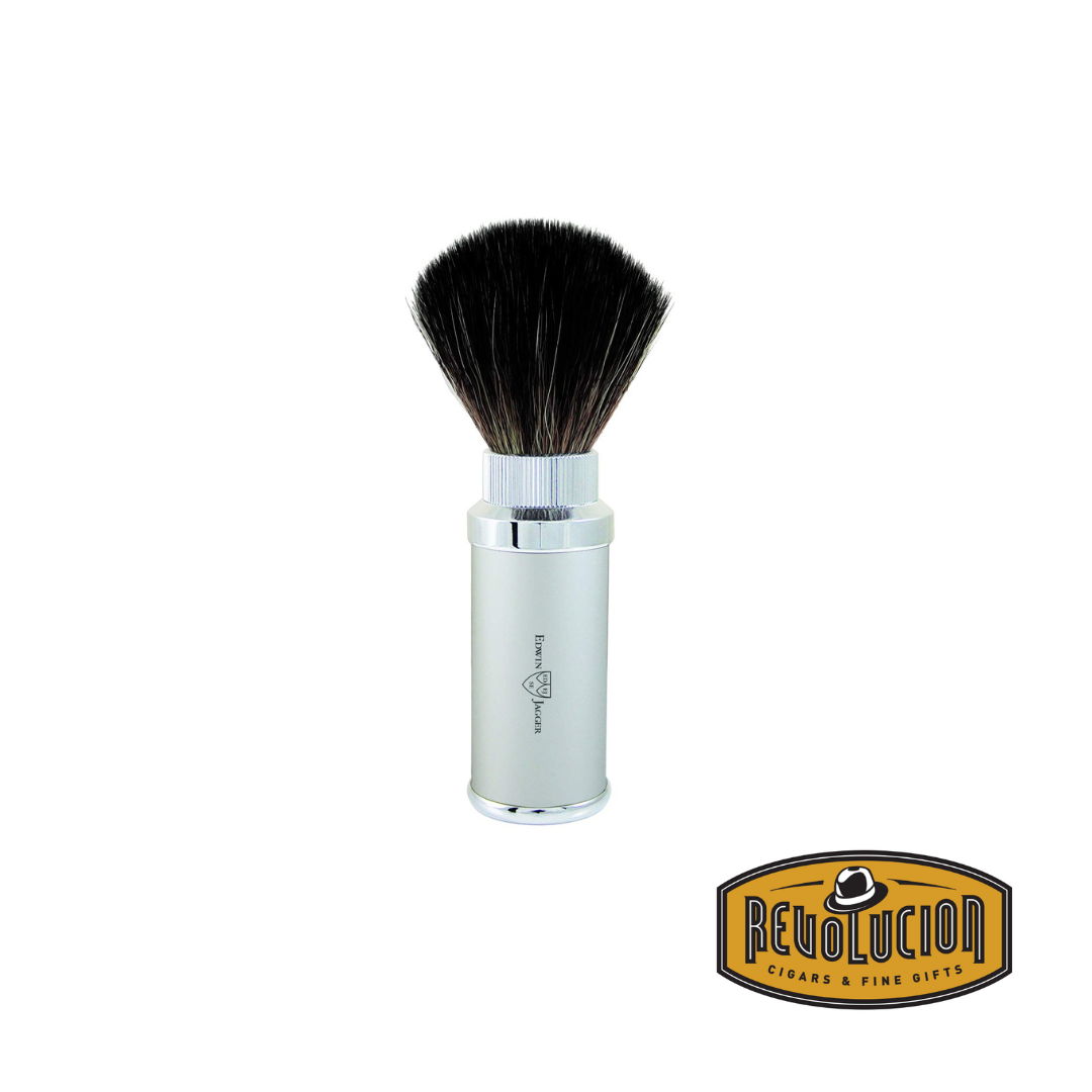 An Edwin Jagger travel shaving brush in chrome silver with the synthetic fiber brush extended. The cylindrical handle has a polished metal finish, and the Edwin Jagger logo is engraved on its side. The Revolucion Cigars & Fine Gifts logo is at the bottom right.