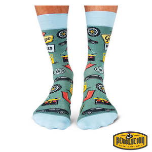 Front view of green socks with light blue cuffs and toes, featuring garage-themed graphics including tools, tires, and cars. The socks are branded with the Revolucion Cigars & Fine Gifts logo