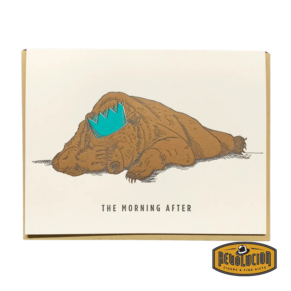 A tired grizzly bear lying flat on the ground wearing a crumpled blue party crown, with the caption “The Morning After.”