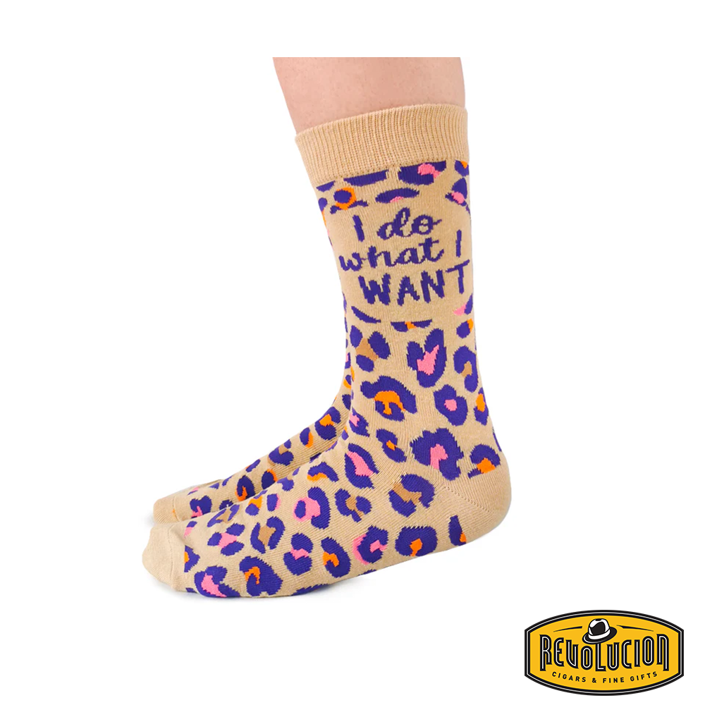 Front view of beige socks with vibrant purple, pink, and orange leopard print pattern. Socks feature the phrase 'I do what I want' and are branded with the Revolucion Cigars & Fine Gifts logo