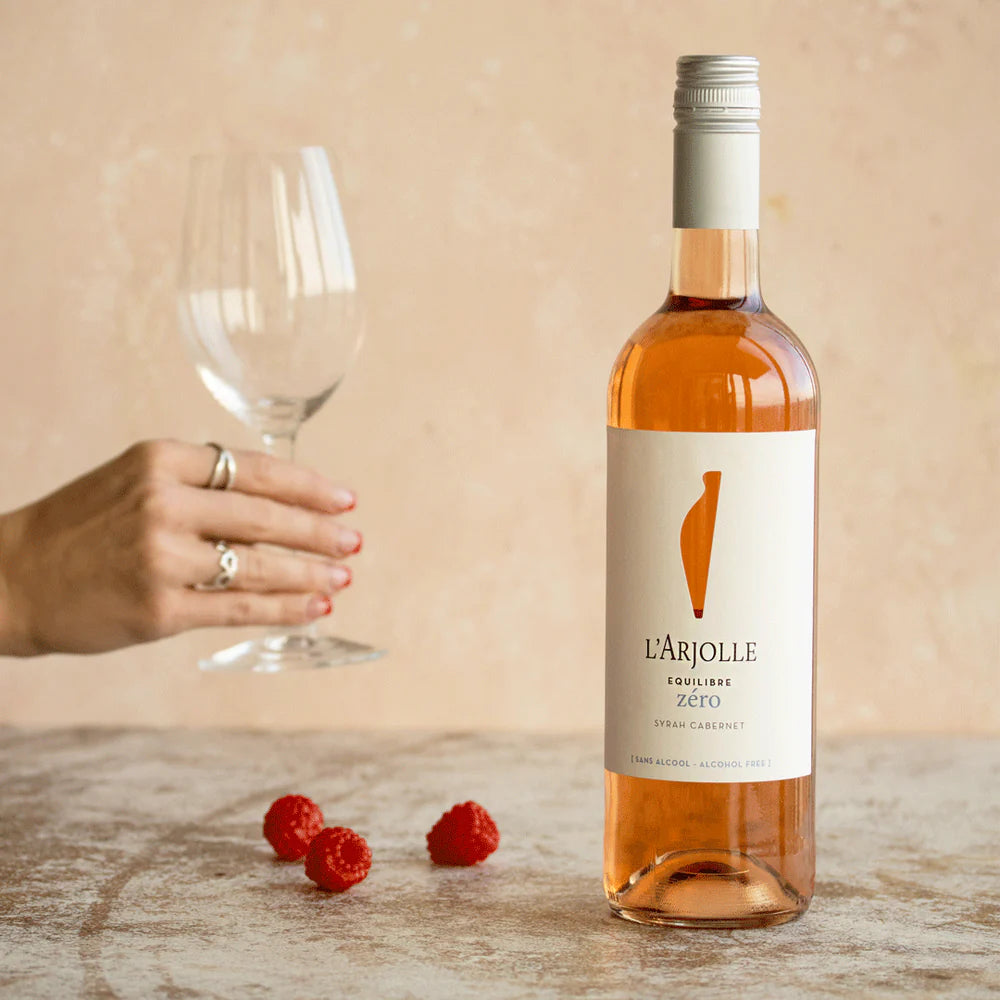 L'Arjolle Syrah Cabernet Rosé Non-Alcoholic 750 ml bottle displayed alongside a glass, illustrating its light pink color and refreshing qualities, perfect for a non-alcoholic rosé experience.
