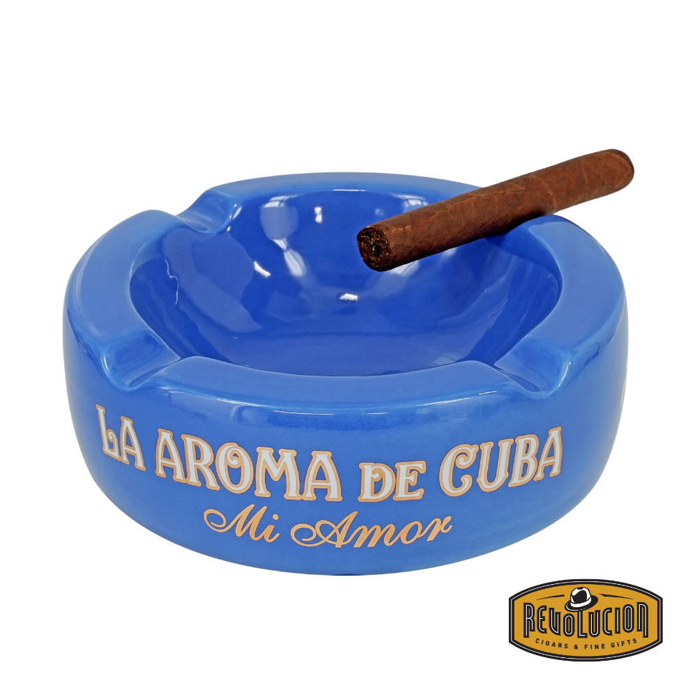 La Aroma de Cuba Mi Amor Ashtray in Blue, featuring a vibrant finish with four cigar grooves and the iconic branding, displayed with a cigar and the Revolucion Cigars &amp; Fine Gifts logo.