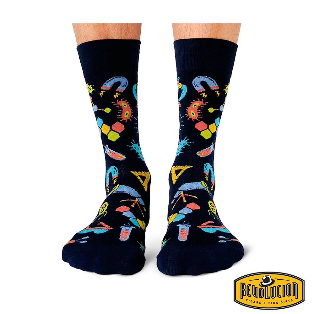 Front view of black socks featuring colorful science-themed graphics including test tubes, molecules, and magnifying glasses. The socks are branded with the Revolucion Cigars &amp; Fine Gifts logo