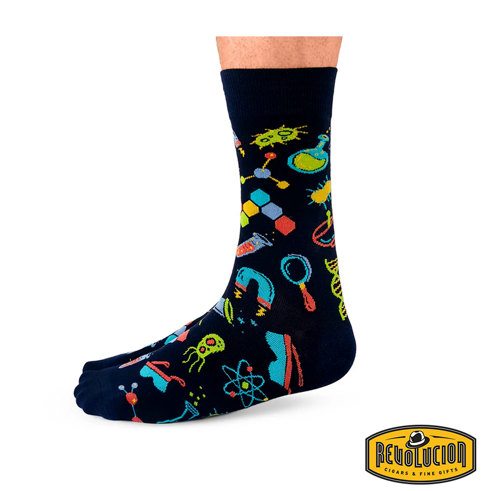 Front view of black socks featuring colorful science-themed graphics including test tubes, molecules, and magnifying glasses. The socks are branded with the Revolucion Cigars & Fine Gifts logo