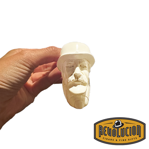 A hand holding a Meerschaum pipe with a carved face of a man with a mustache, wearing a hat. The pipe is cream-colored and intricately detailed.