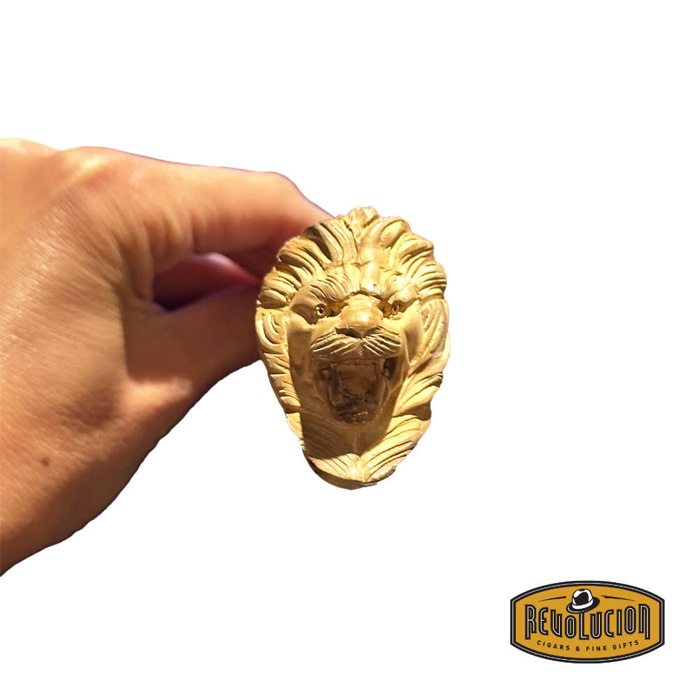 A hand holding a Meerschaum smoking pipe with a detailed lion head carving at the front. The intricate lattice finish adds a sophisticated touch to the cream-colored bowl.