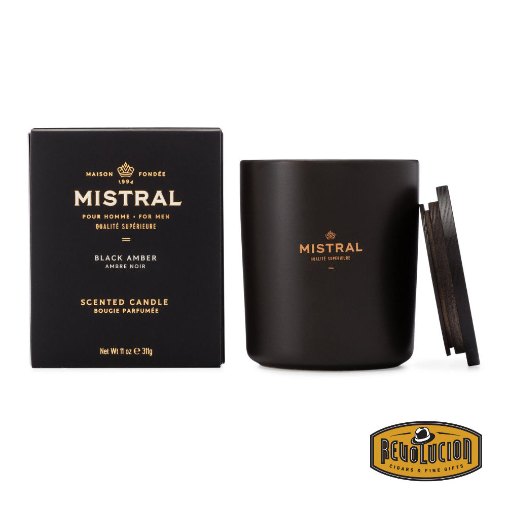 Black Mistral candle in an elegant black jar with a wooden lid, featuring the label ‘Black Amber - Pour Homme’ and a matching box showcasing the same branding. The image includes the Revolucion Cigars &amp; Fine Gifts logo