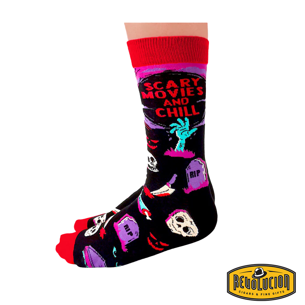 Front view of colorful socks with 'Scary Movies and Chill' theme, featuring skeletons, tombstones, and horror elements. Socks are black with red cuffs and toes, branded with the Revolucion Cigars & Fine Gifts logo