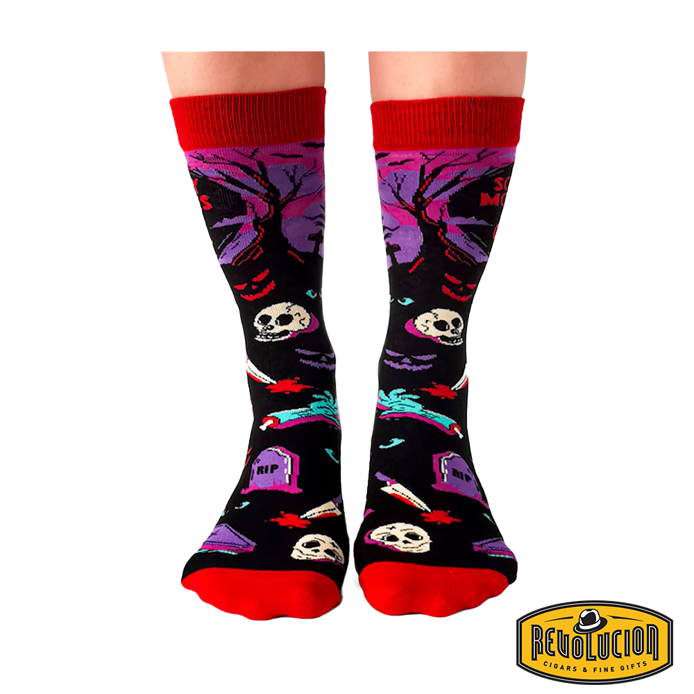 Front view of colorful socks with &#39;Scary Movies and Chill&#39; theme, featuring skeletons, tombstones, and horror elements. Socks are black with red cuffs and toes, branded with the Revolucion Cigars &amp; Fine Gifts logo