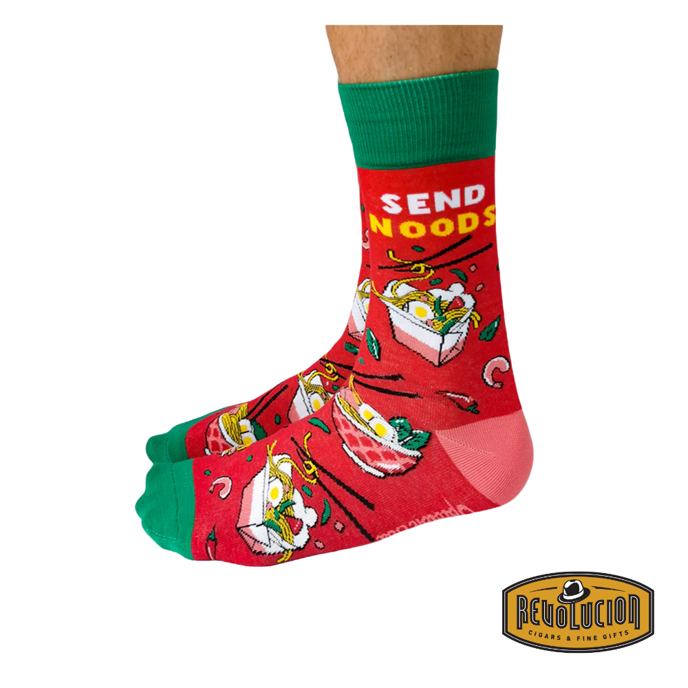 Side view of red socks featuring playful noodle graphics and the phrase 'Send Noods' in bold yellow letters. The socks have green cuffs, green toes, and pink heels, branded with the Revolucion Cigars & Fine Gifts logo.