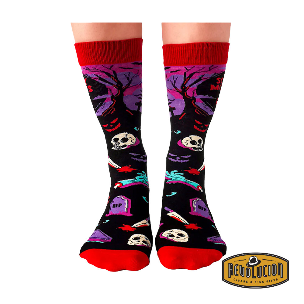 Front view of colorful socks with 'Scary Movies and Chill' theme, featuring skeletons, tombstones, and horror elements. Socks are black with red cuffs and toes, branded with the Revolucion Cigars & Fine Gifts logo.