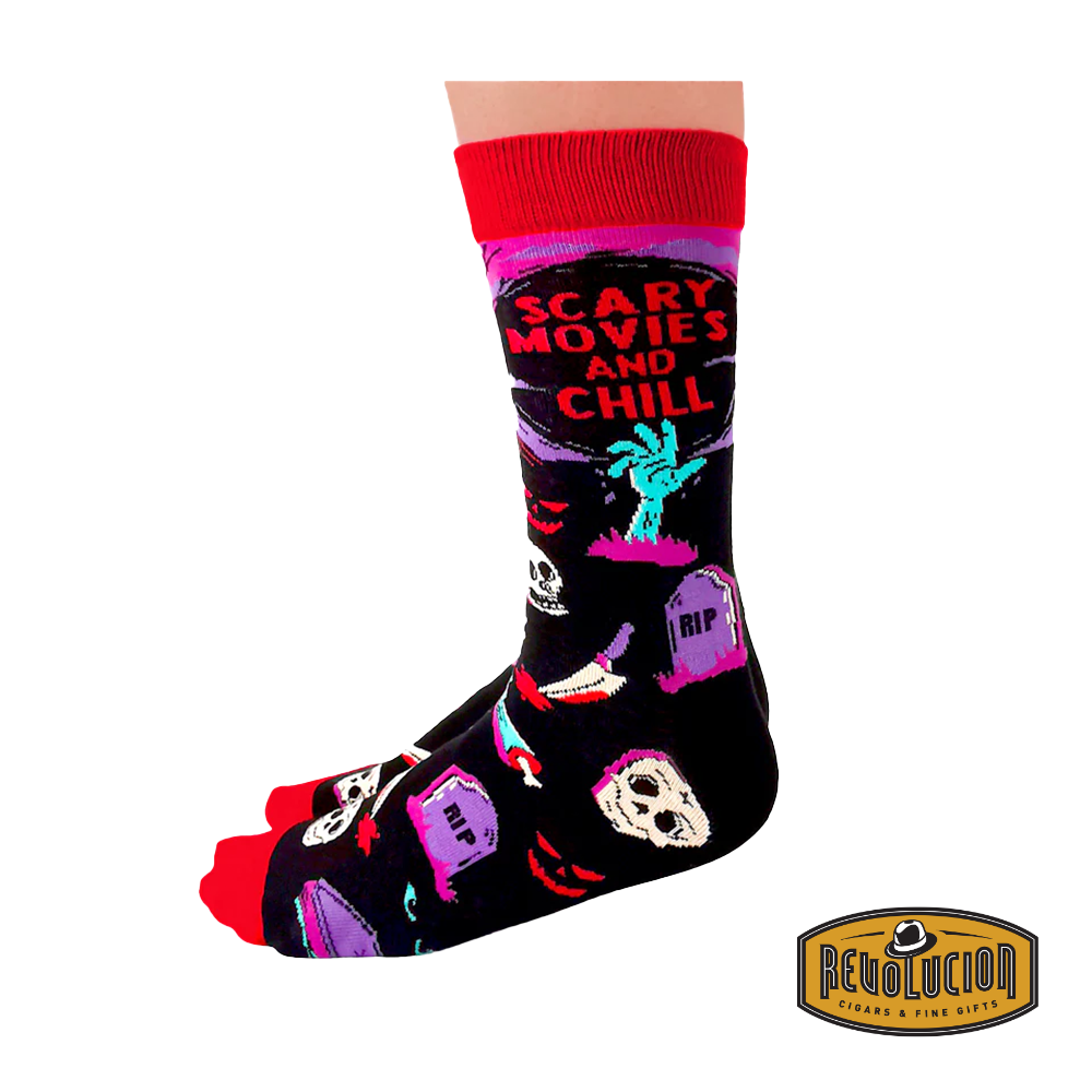 Side view of socks with 'Scary Movies and Chill' theme, showcasing detailed graphics of skeletons, tombstones, and horror elements. Socks are black with red cuffs and toes, branded with the Revolucion Cigars & Fine Gifts logo.
