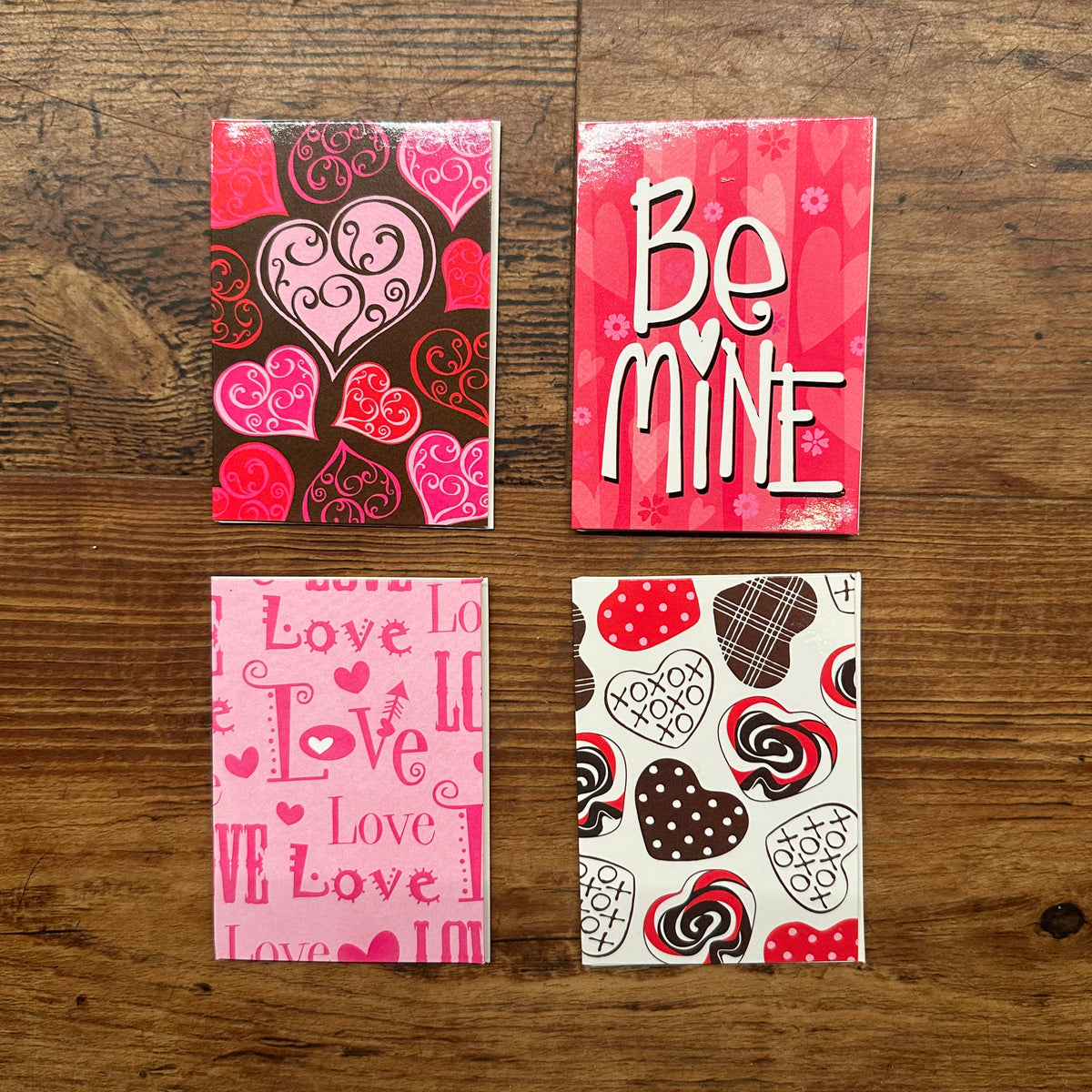 A layout of 4 printed Valentines Day themed cards in pink, red and black that read out &quot;be mine&quot; and &#39;love&#39;. Available to purchase online at revolucion cigars and fine gifts shop located in Vancouver, Bc Canada.