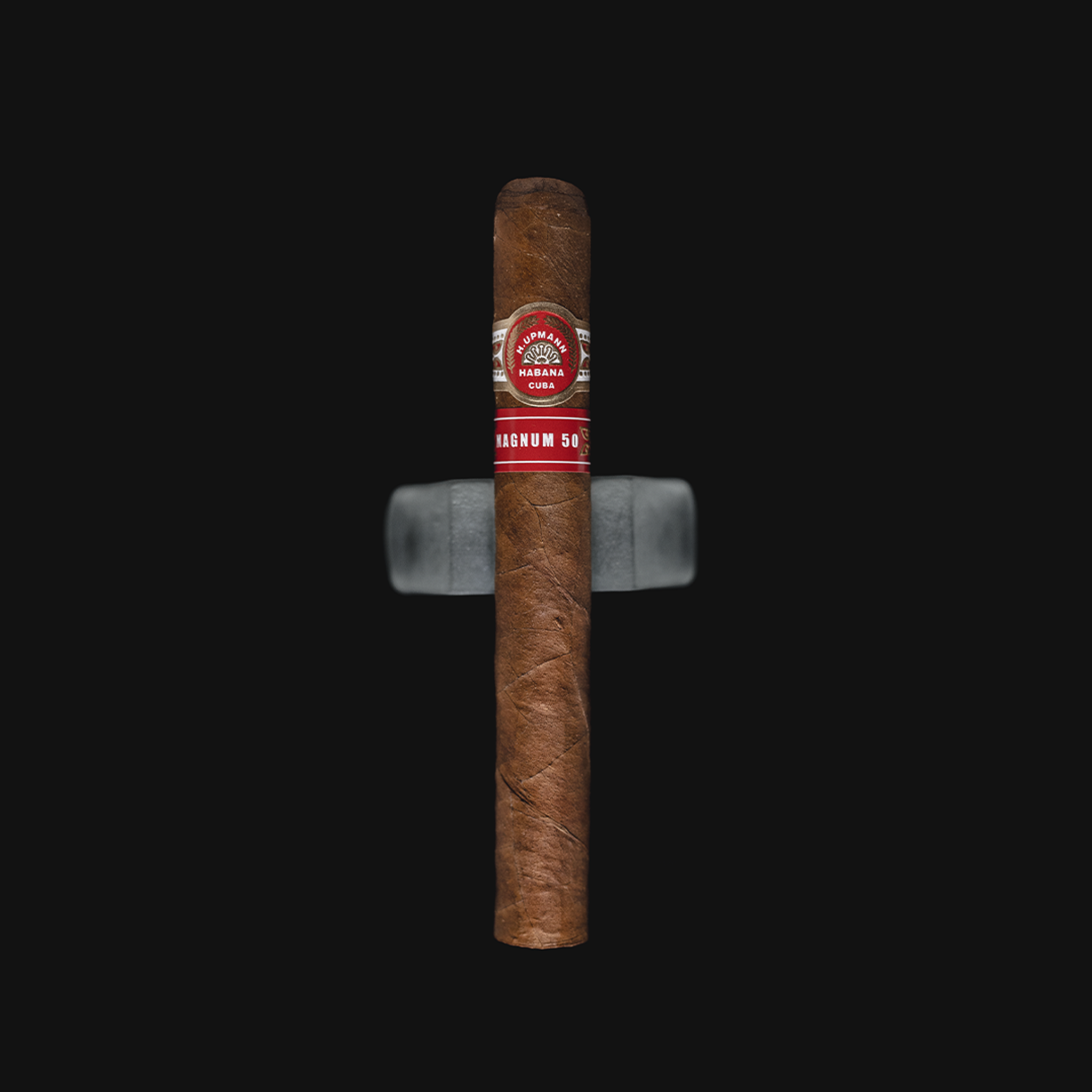 H. Upmann Magnum 50 Cuban cigar with a red and gold band, placed on a dark background.