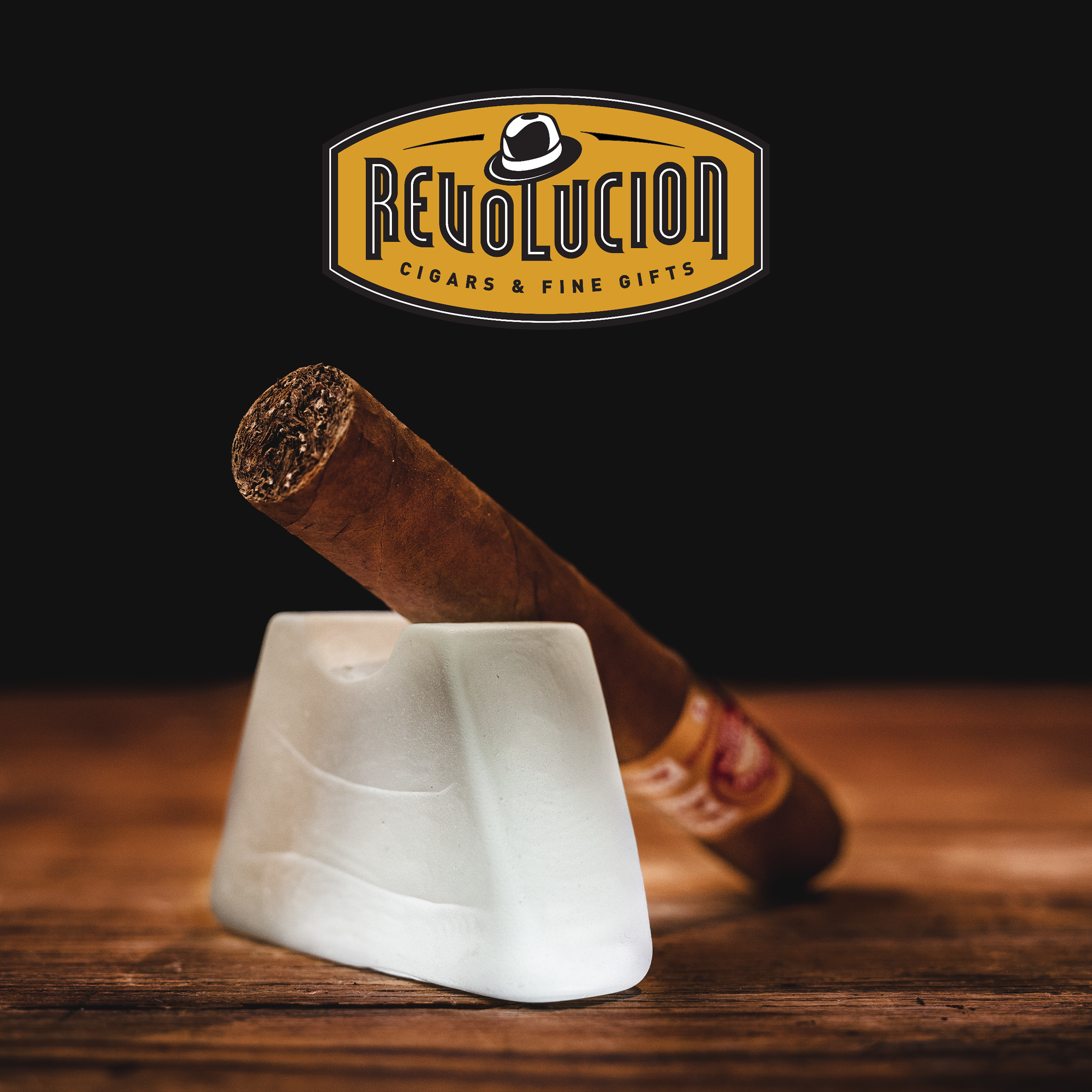 H. Upmann Connossieur No. 2 Cuban cigar resting on a glass stand with the Revolucion Cigars & Fine Gifts logo in the background.
