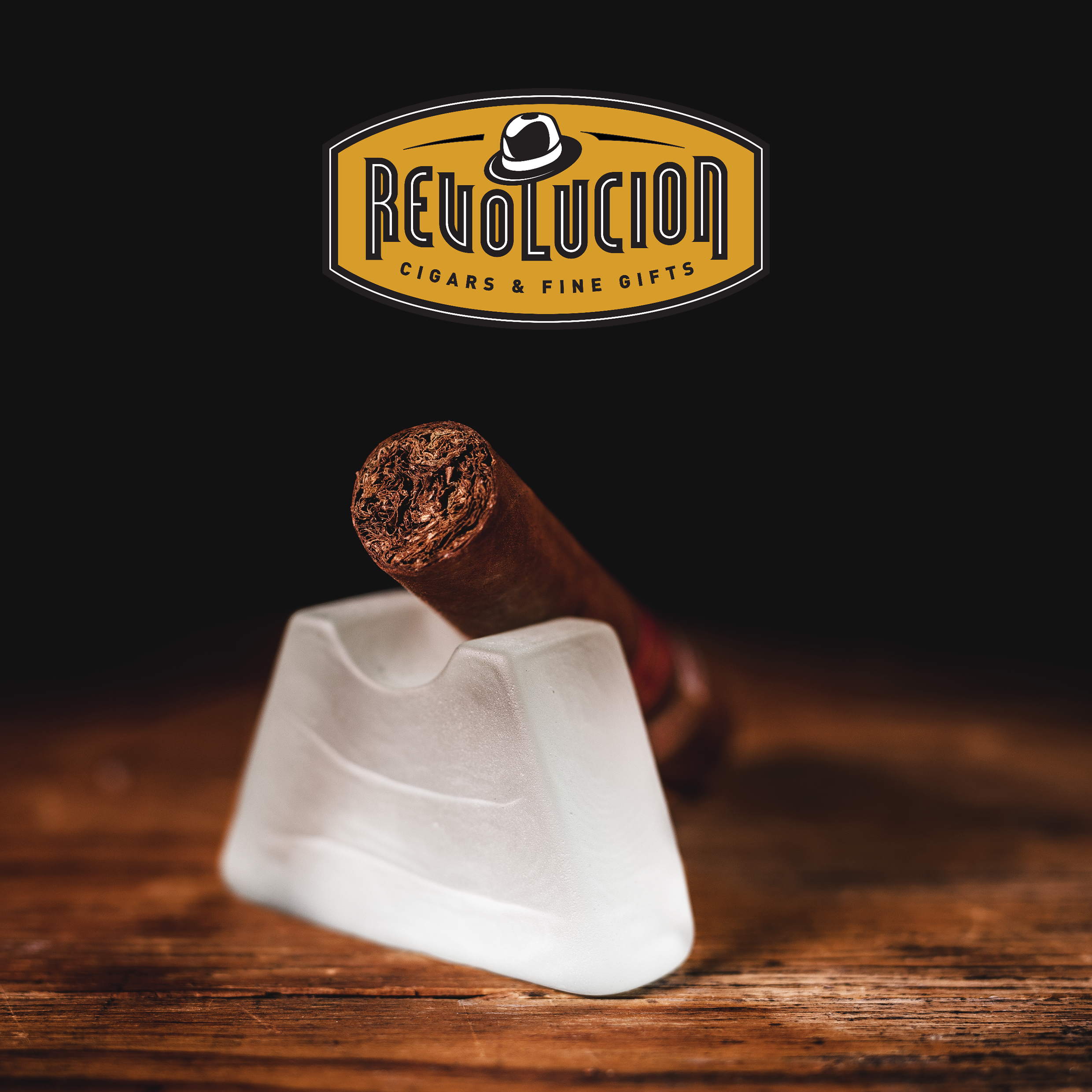 H. Upmann Magnum 54 Cuban cigar showing the foot on a frosted glass stand, with the Revolucion Cigars & Fine Gifts logo above, set against a dark background.