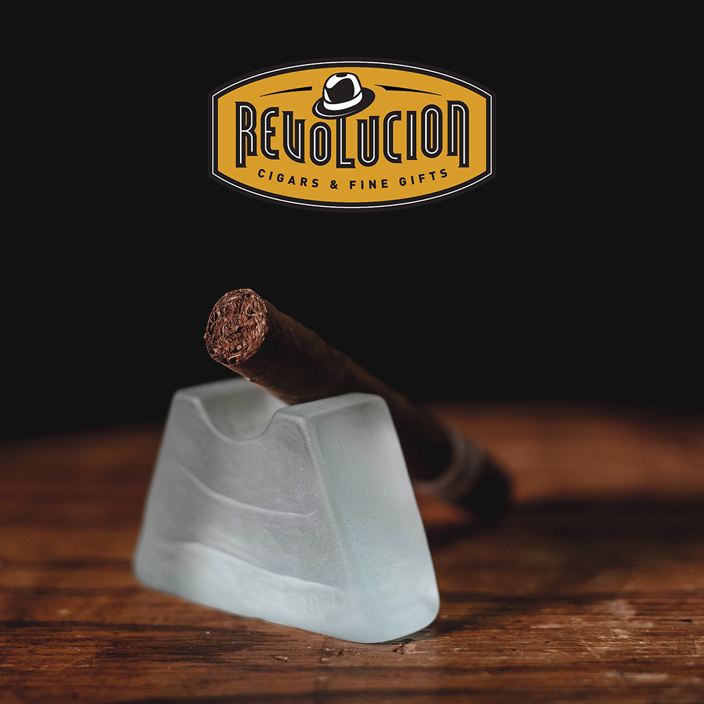 José L. Piedra Petit Cetros medium-strength Cuban cigar resting on a frosted glass, displayed on a wooden surface with a black background.
