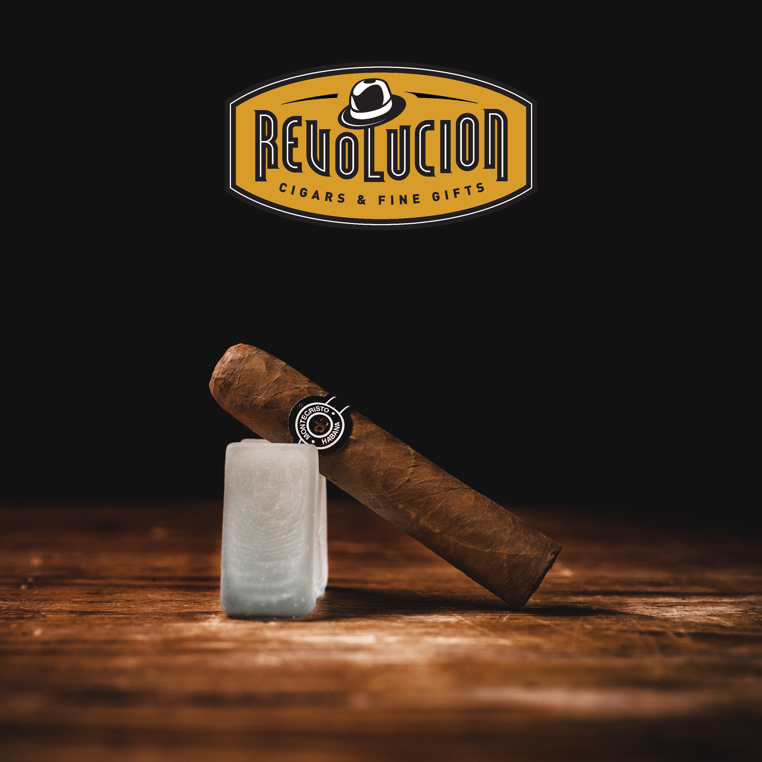 Montecristo Petit Edmundo Cuban cigar with a brown and white band, placed on a glass object with a dark background.