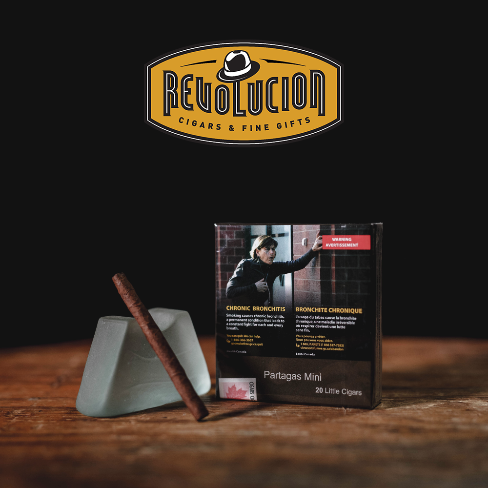 Partagas Mini Full-Strength Cuban Cigarillo next to its plain packaging box, highlighting its size and presentation.