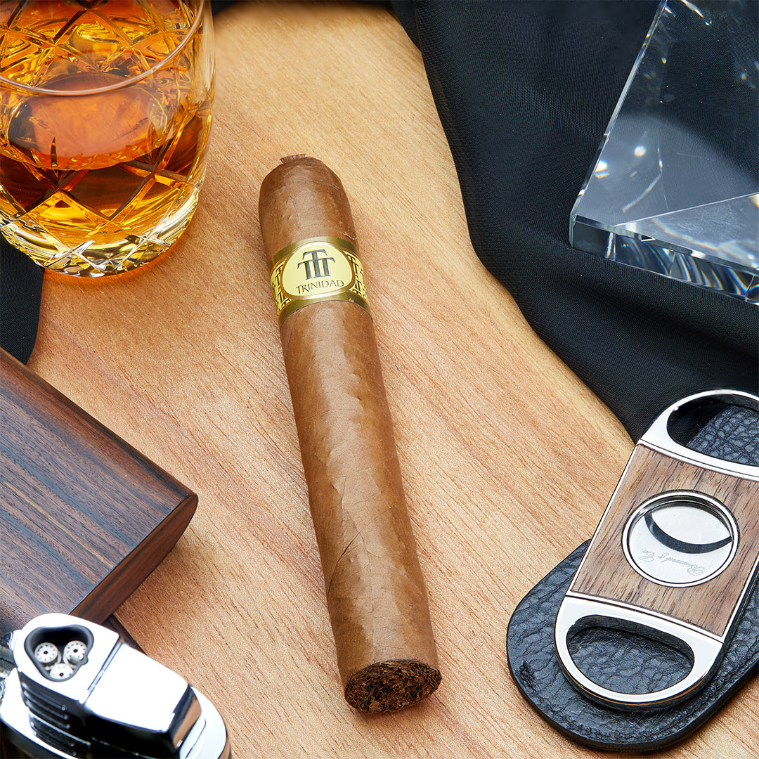 Trinidad Esmeralda Cuban cigar standing vertically on a frosted glass stand against a wood background, featuring its signature pigtail cap and gold band.